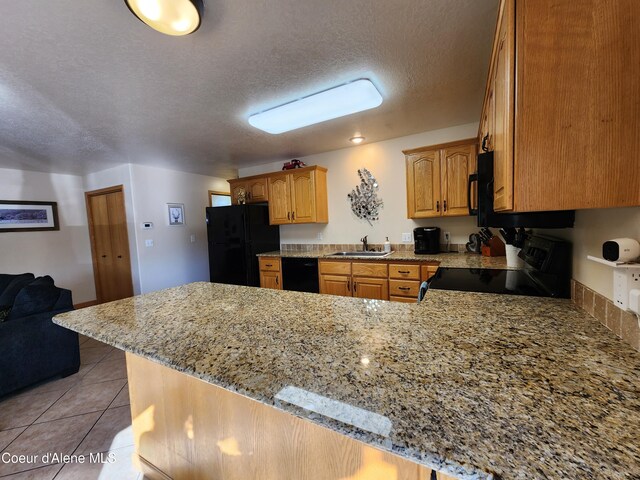 kitchen featuring black appliances, sink, light stone countertops, light tile patterned flooring, and kitchen peninsula