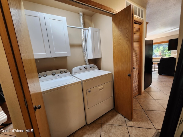 clothes washing area with cabinets, a textured ceiling, light tile patterned flooring, and washing machine and clothes dryer