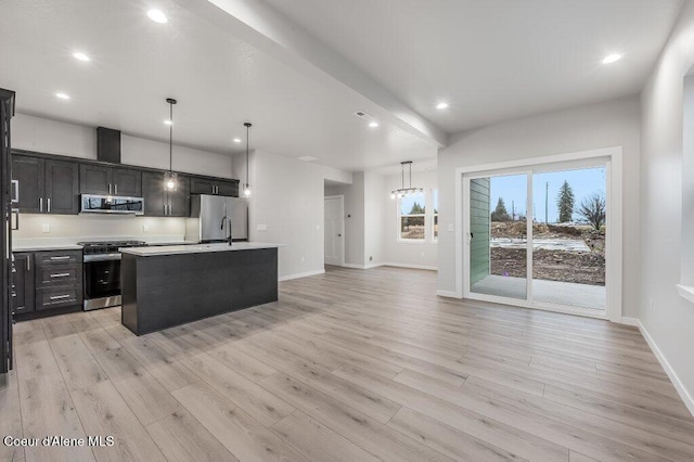 kitchen with hanging light fixtures, appliances with stainless steel finishes, light wood-type flooring, and a kitchen island with sink