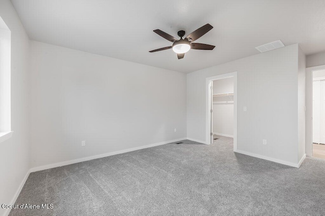 unfurnished bedroom featuring a closet, a walk in closet, light colored carpet, and ceiling fan