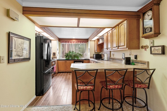 kitchen featuring a kitchen breakfast bar, black fridge, dark hardwood / wood-style flooring, kitchen peninsula, and crown molding