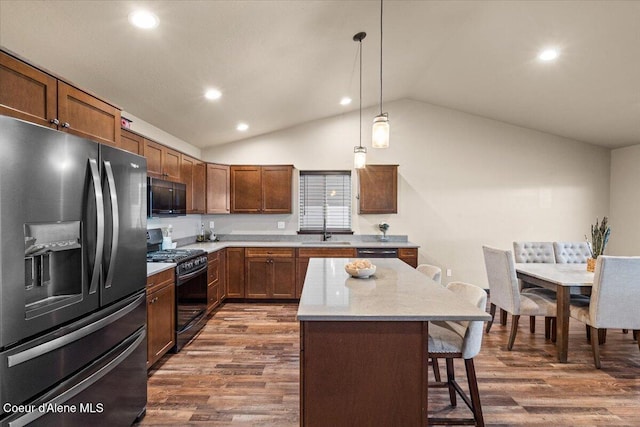 kitchen with vaulted ceiling, dark wood-type flooring, black appliances, pendant lighting, and a kitchen island