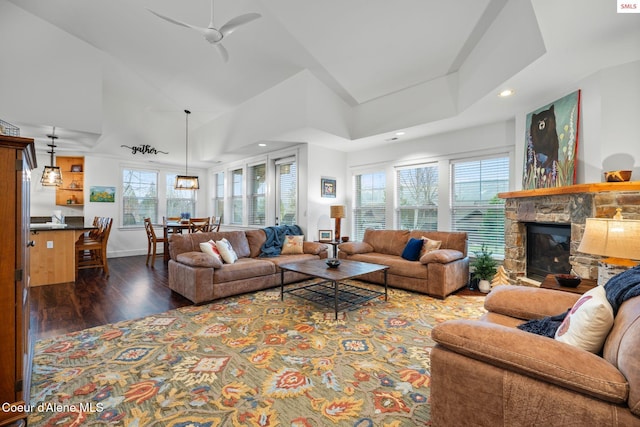 living room featuring dark wood-type flooring, a stone fireplace, ceiling fan, and a healthy amount of sunlight