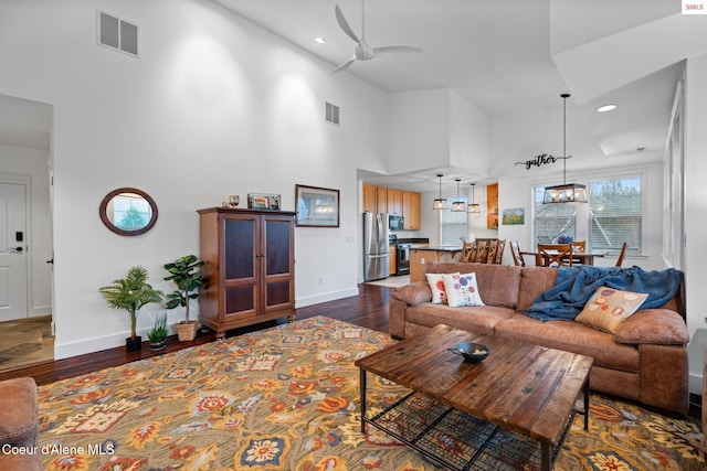 living room featuring ceiling fan with notable chandelier, dark hardwood / wood-style flooring, and a towering ceiling