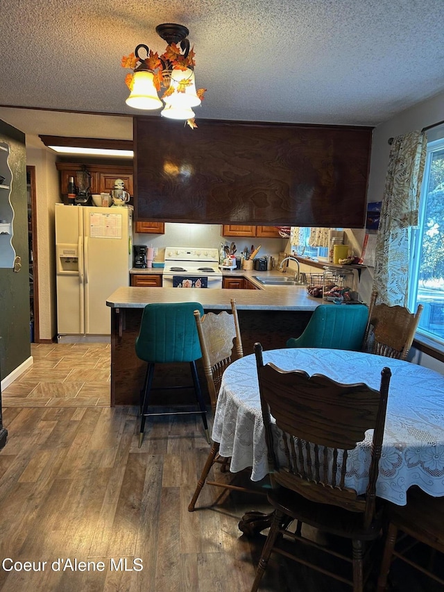 dining area with a textured ceiling, light wood-type flooring, an inviting chandelier, and sink