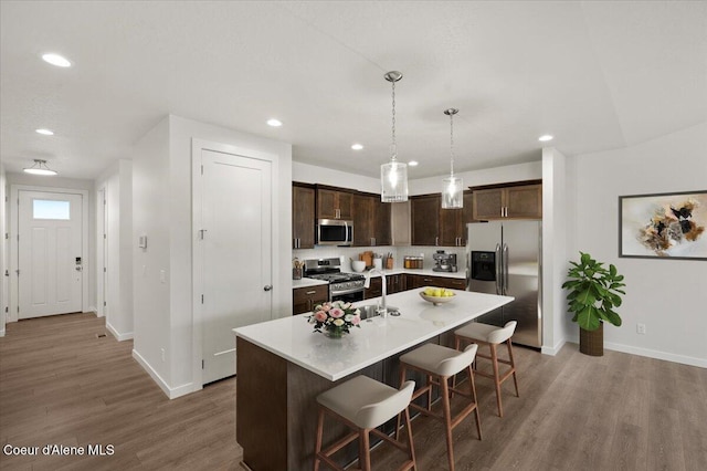 kitchen featuring a center island with sink, a kitchen breakfast bar, stainless steel appliances, and hardwood / wood-style floors