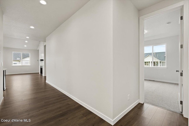 corridor featuring vaulted ceiling, plenty of natural light, dark wood-type flooring, and a textured ceiling