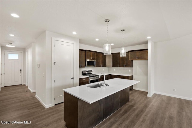 kitchen with sink, dark hardwood / wood-style floors, an island with sink, pendant lighting, and appliances with stainless steel finishes