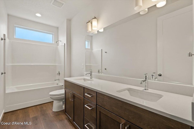 full bathroom featuring washtub / shower combination, hardwood / wood-style floors, a textured ceiling, toilet, and vanity