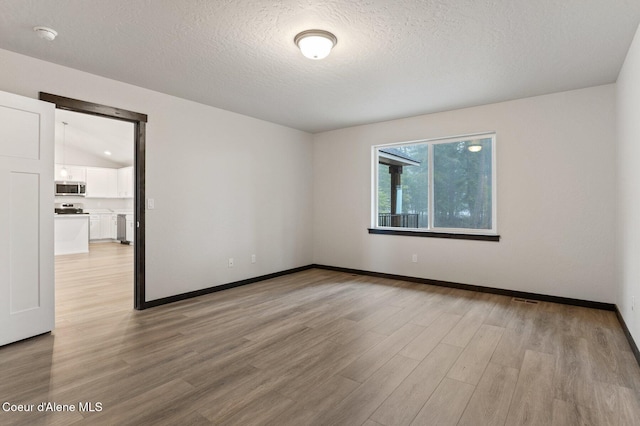 empty room with light hardwood / wood-style floors, a textured ceiling, and vaulted ceiling