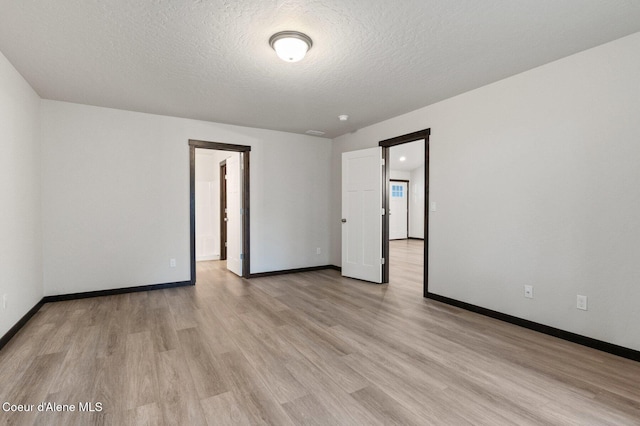 empty room with a textured ceiling and light hardwood / wood-style flooring