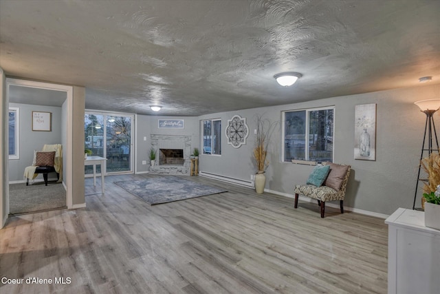 unfurnished living room with a textured ceiling, baseboard heating, and light hardwood / wood-style flooring