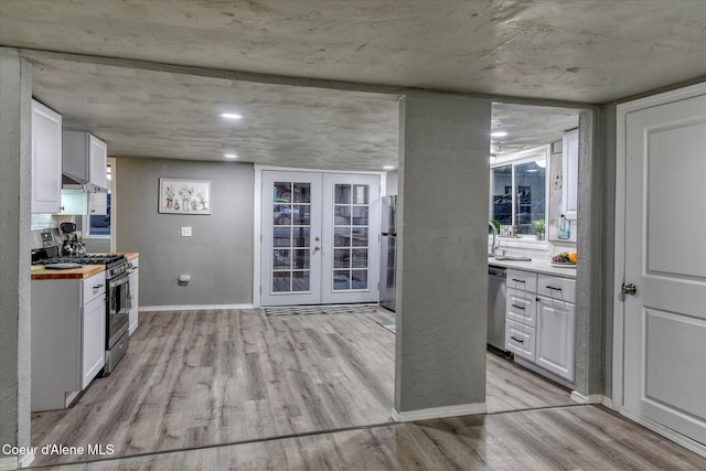 kitchen featuring wood counters, appliances with stainless steel finishes, light wood-type flooring, french doors, and white cabinetry