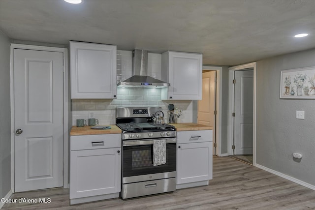 kitchen featuring wall chimney range hood, white cabinetry, wood counters, and stainless steel gas range