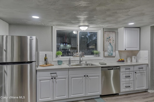 kitchen with white cabinets, appliances with stainless steel finishes, light hardwood / wood-style floors, and sink