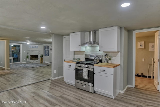 kitchen featuring butcher block countertops, white cabinetry, wall chimney exhaust hood, and stainless steel range with gas stovetop