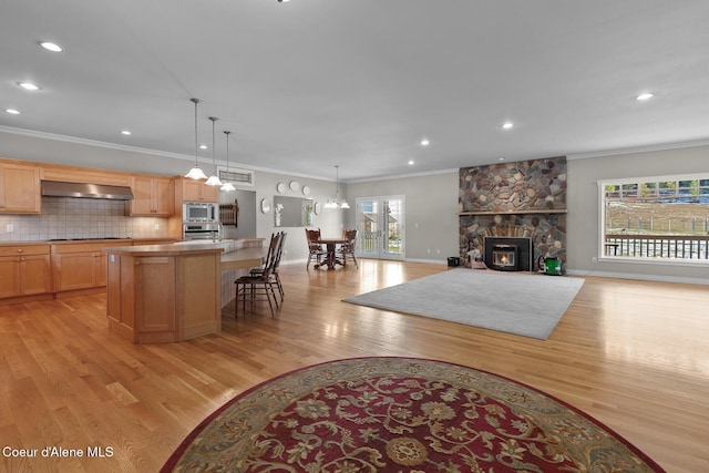 kitchen with light wood-type flooring, ventilation hood, a kitchen island, and stainless steel appliances