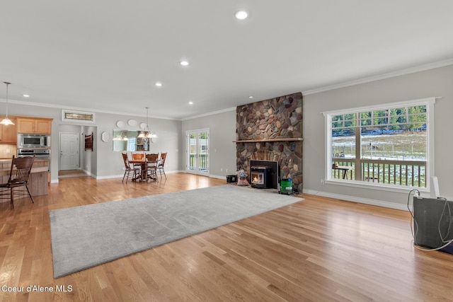 living room featuring a stone fireplace, light hardwood / wood-style flooring, a healthy amount of sunlight, and crown molding