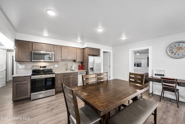 kitchen with appliances with stainless steel finishes, light wood-type flooring, backsplash, dark brown cabinetry, and sink