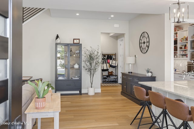 bar featuring light wood-type flooring, light stone counters, hanging light fixtures, and a notable chandelier