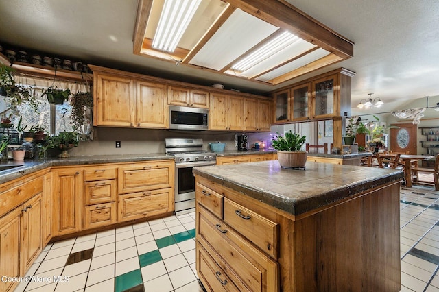 kitchen with stainless steel appliances, a kitchen island, a notable chandelier, tile countertops, and light tile patterned flooring