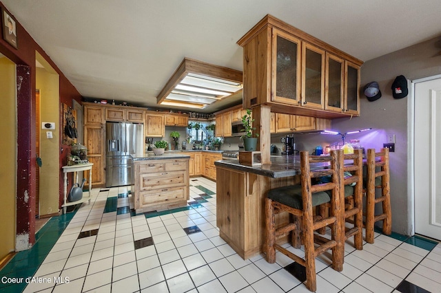 kitchen featuring kitchen peninsula, light tile patterned floors, stainless steel appliances, and a breakfast bar area