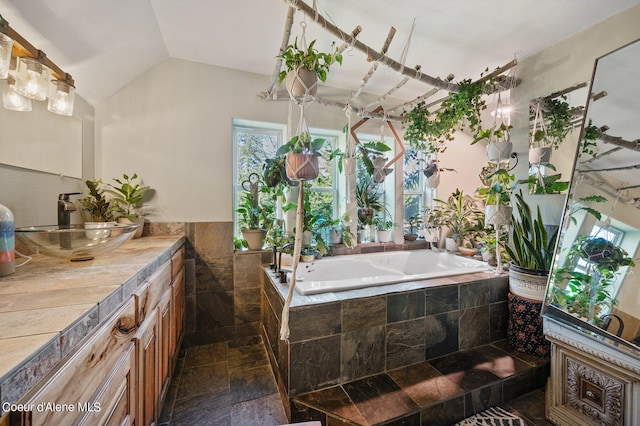 bathroom featuring vanity, a relaxing tiled tub, vaulted ceiling, and tile walls