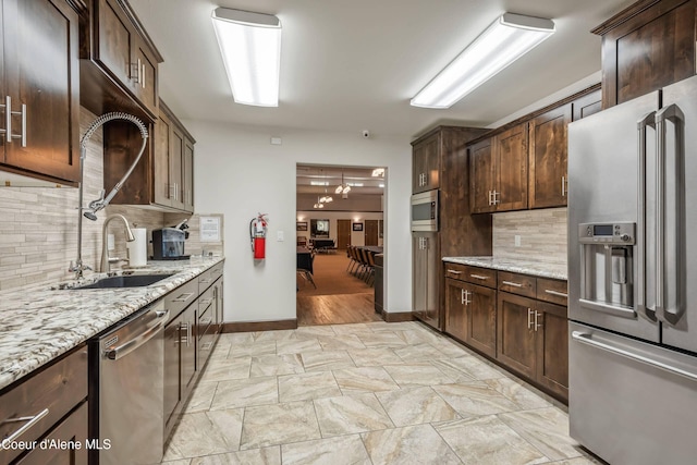 kitchen with dark brown cabinets, stainless steel appliances, light stone counters, and tasteful backsplash