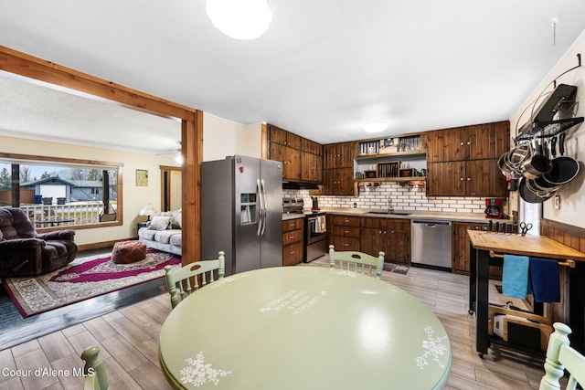 kitchen with tasteful backsplash, dark brown cabinets, stainless steel appliances, sink, and light hardwood / wood-style floors