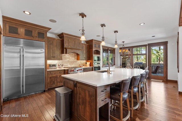 6126 S Gozzer Rd, Harrison, ID 83833 - kitchen with dark wood-type flooring, hanging light fixtures, backsplash, built in appliances, and an island with sink