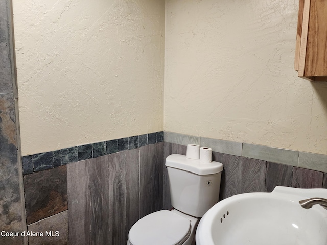 bathroom featuring toilet, tile walls, and sink