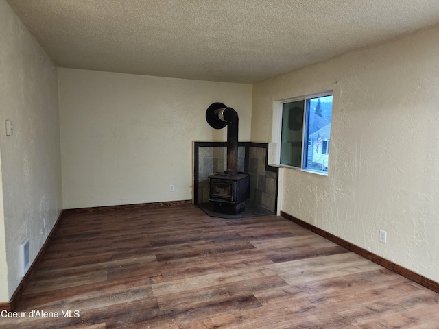 unfurnished living room featuring hardwood / wood-style flooring, a wood stove, and a textured ceiling