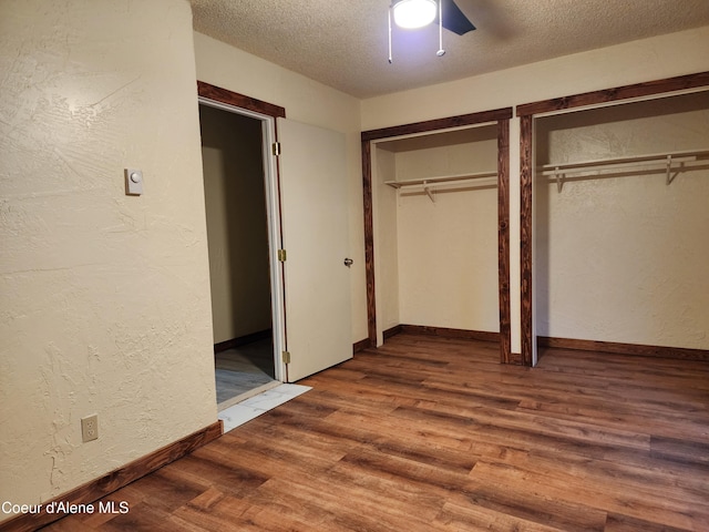 unfurnished bedroom featuring two closets, ceiling fan, wood-type flooring, and a textured ceiling