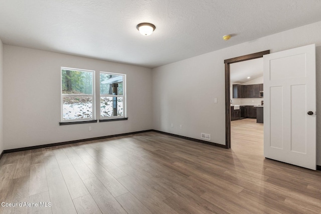 spare room with a textured ceiling, light hardwood / wood-style floors, and lofted ceiling