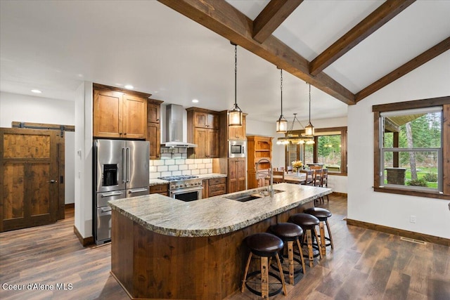 kitchen featuring hanging light fixtures, sink, wall chimney exhaust hood, a barn door, and appliances with stainless steel finishes