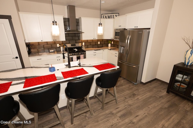 kitchen featuring decorative light fixtures, white cabinetry, wall chimney range hood, and appliances with stainless steel finishes