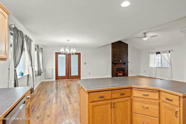 kitchen featuring stainless steel dishwasher, a fireplace, a kitchen island, ceiling fan with notable chandelier, and light wood-type flooring