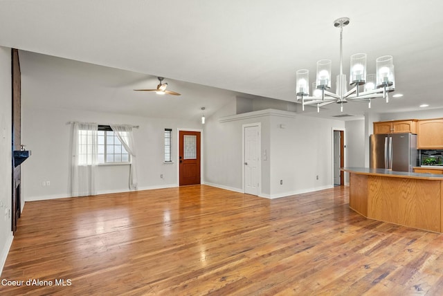 unfurnished living room featuring ceiling fan with notable chandelier, vaulted ceiling, and light hardwood / wood-style flooring