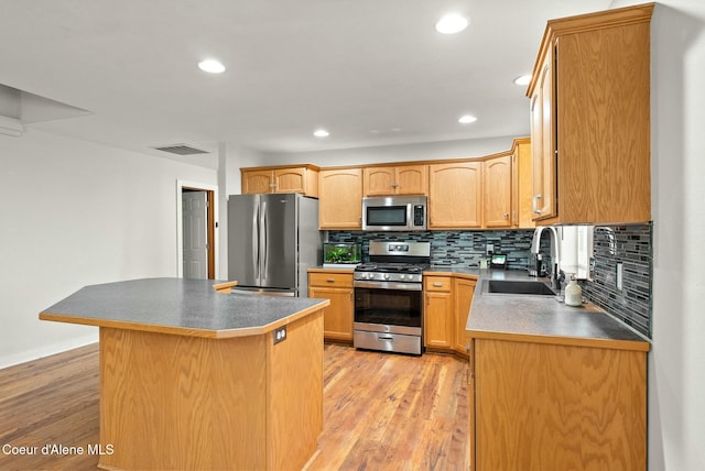 kitchen with decorative backsplash, appliances with stainless steel finishes, light wood-type flooring, sink, and a kitchen island