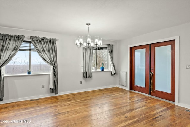 unfurnished dining area with hardwood / wood-style floors, french doors, and an inviting chandelier