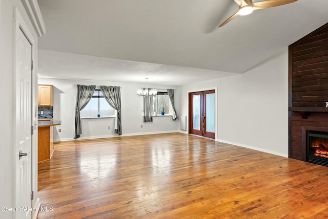 unfurnished living room featuring french doors, ceiling fan with notable chandelier, vaulted ceiling, light hardwood / wood-style floors, and a large fireplace