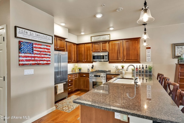 kitchen with sink, kitchen peninsula, decorative light fixtures, high quality appliances, and a breakfast bar