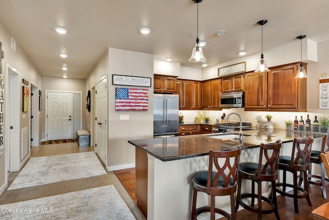 kitchen with kitchen peninsula, appliances with stainless steel finishes, a breakfast bar, sink, and decorative light fixtures