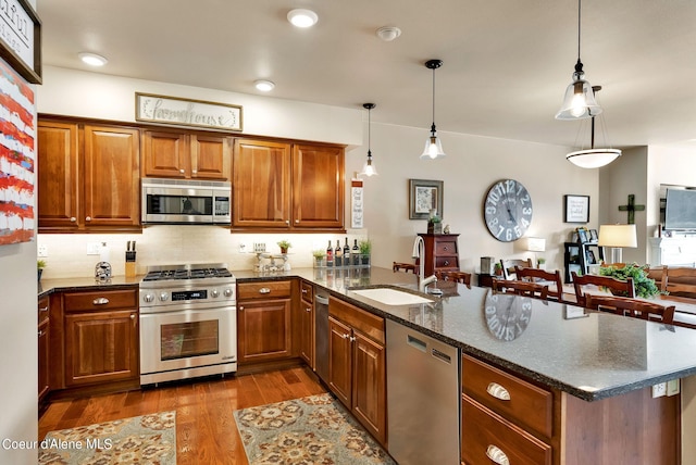 kitchen with sink, dark hardwood / wood-style flooring, dark stone countertops, decorative light fixtures, and appliances with stainless steel finishes