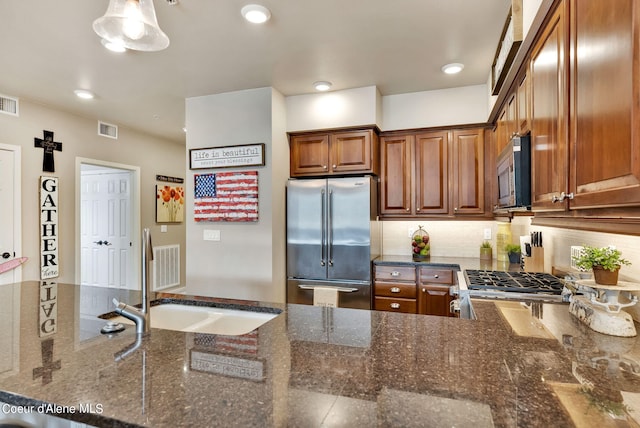 kitchen with dark stone countertops, stove, sink, and stainless steel refrigerator