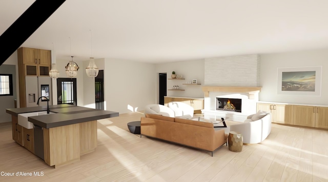 living room featuring a large fireplace, light hardwood / wood-style floors, sink, and a chandelier