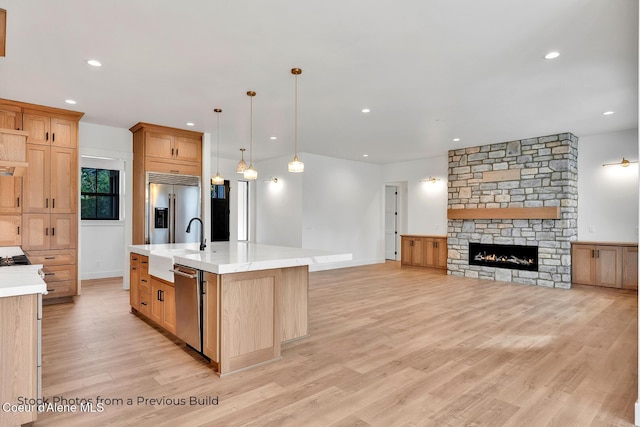 kitchen featuring appliances with stainless steel finishes, pendant lighting, a fireplace, light hardwood / wood-style floors, and a large island