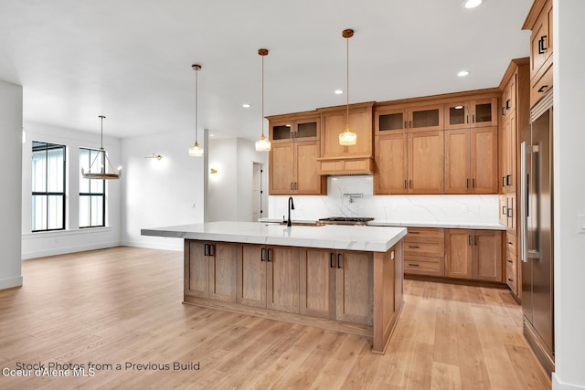 kitchen featuring sink, light wood-type flooring, hanging light fixtures, and an island with sink