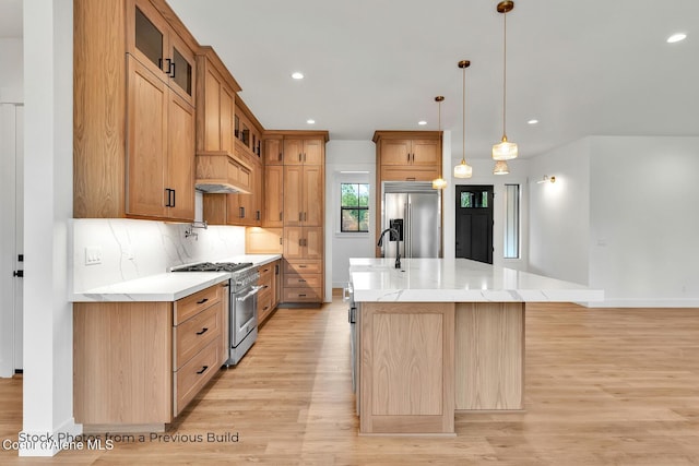 kitchen with light stone counters, premium appliances, a large island with sink, decorative light fixtures, and light hardwood / wood-style floors