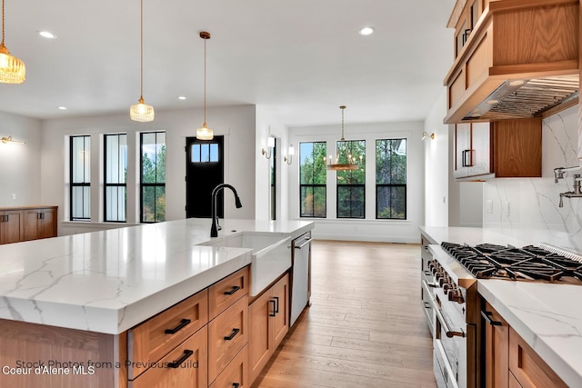 kitchen featuring pendant lighting, light stone countertops, a large island with sink, and appliances with stainless steel finishes